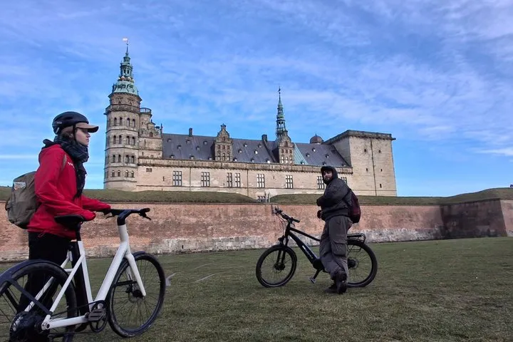 Two riders with e-bikes on the grass outside Kronborg on an e-bike tour to Hamlet Castle